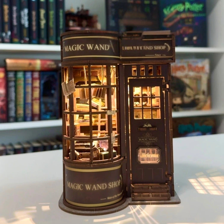 Assembled Magic Wand Shop book nook with warm light, displayed on a bookshelf next to fantasy novels.