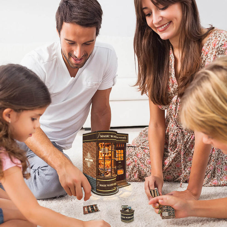 Family smiling and building the Magic Wand Shop kit together on the floor.