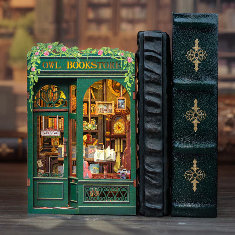 The Owl Bookstore book nook inserted between two large, leather-bound books on a bookshelf, showing its decorative use.